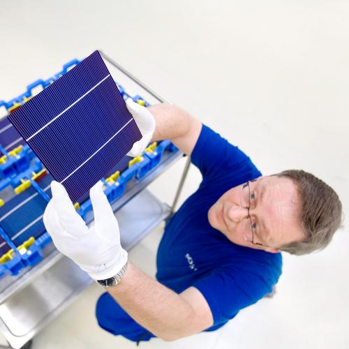 Mitarbeiter betrachtet eine fertige Solarzelle.